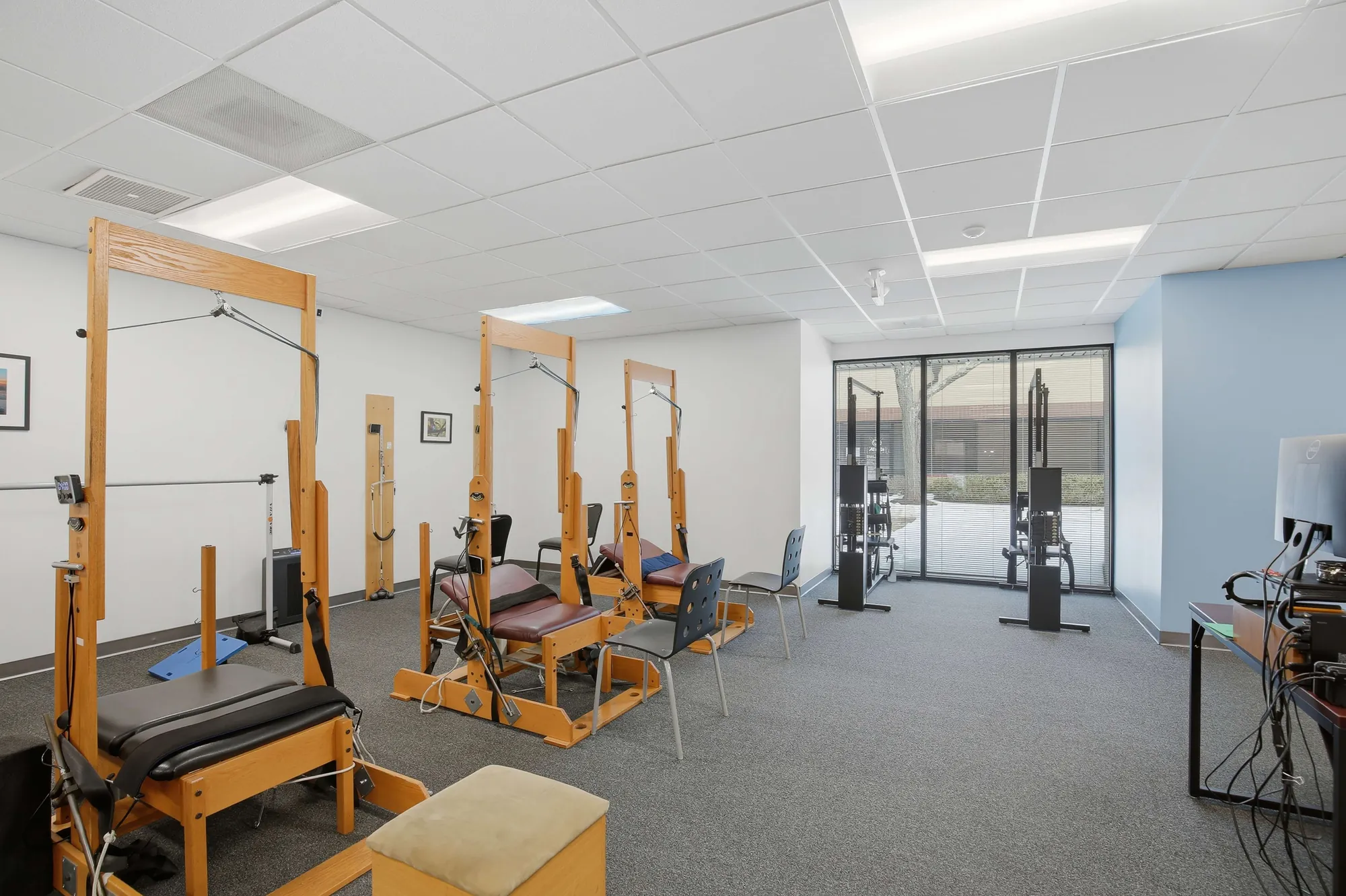 Open rehab room with wooden pilates-style reformer machines and cable stations.