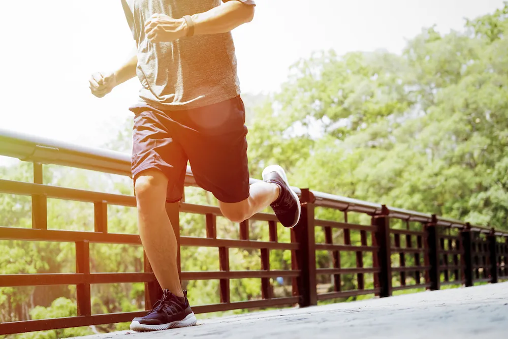 Jogger in shorts and sneakers running across a bridge among trees.