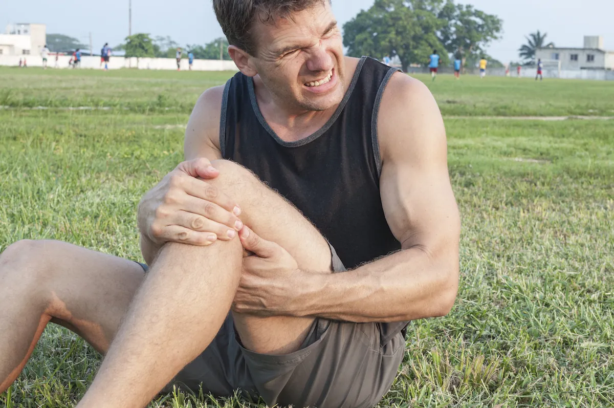 Man sitting on grass grimacing and clutching his knee.