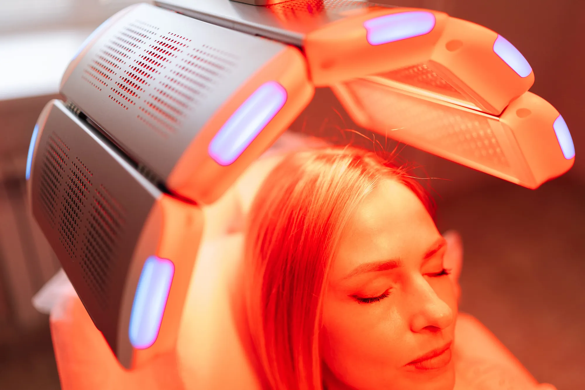 Woman rests under a red light therapy panel with glowing red illumination.