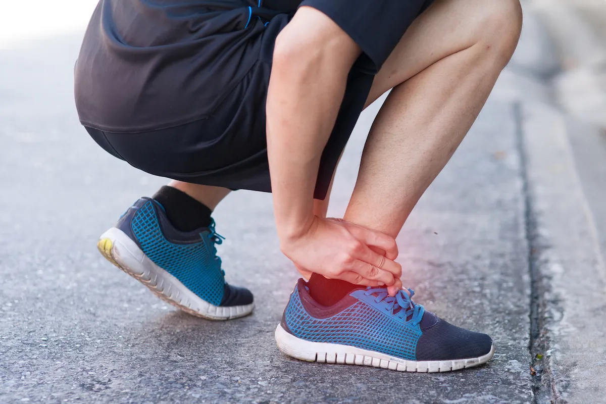 Runner crouching on a road and holding his painful ankle.