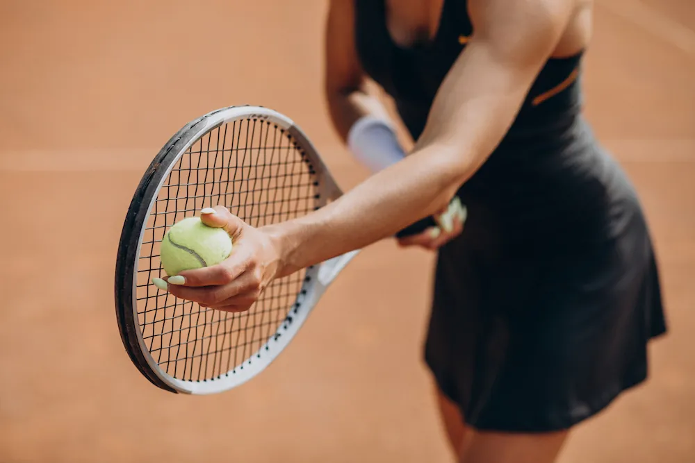 Tennis player holding a ball and racket, preparing to serve on a clay court.