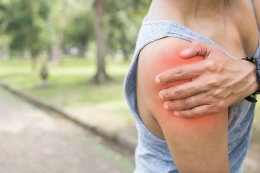 Woman outdoors holding her upper arm with the shoulder highlighted in red.